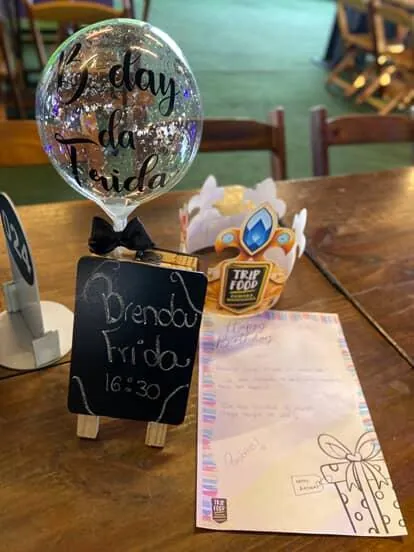 Mesa de aniversário montada no Trip Food com balão personalizado, plaquinha de lousa, coroa da casa e cartão escrito à mão